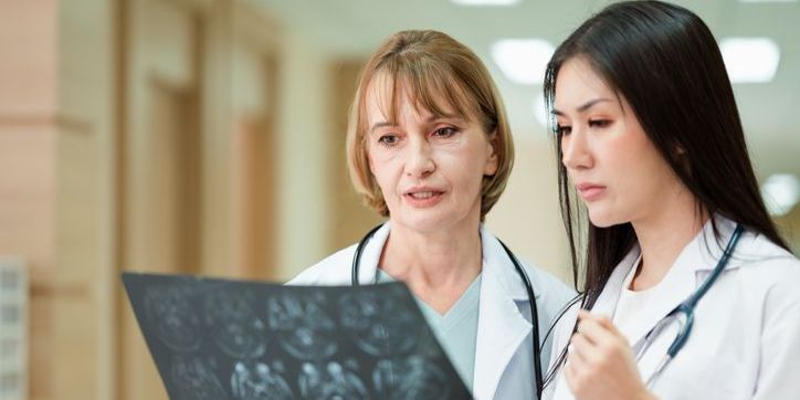 Doctor in uniform, a stethoscope, and a female assistant stand together in a hospital corridor. Consulting or checking the X-ray result sheet