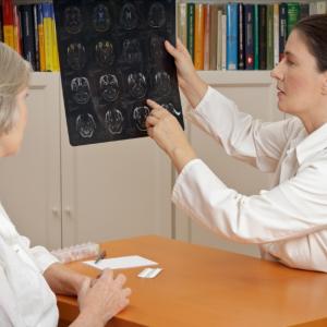 two women wearing white shirts sitting down at a table. The women on the right is holding an image of brain scans 